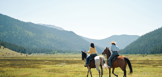 Mountains in the distance and two people riding horses